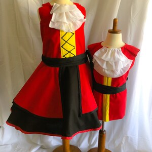 May include: Two red and black pirate costumes with white ruffled collars and yellow accents. The costumes are displayed on wooden mannequins.