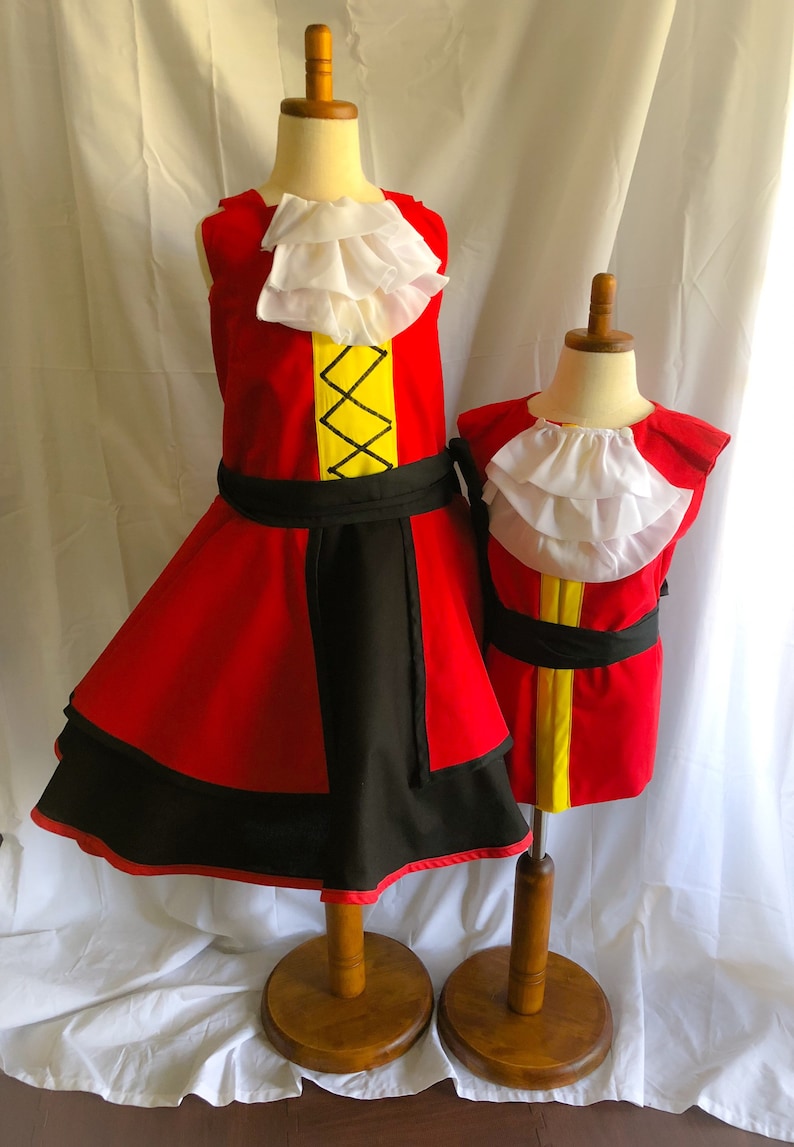 May include: Two red and black pirate costumes with white ruffled collars and yellow accents. The costumes are displayed on wooden mannequins.