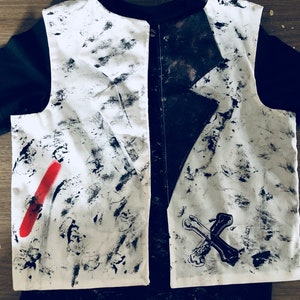 May include: A white vest with black paint splatters and a red stripe on the left side. The vest is paired with a black t-shirt with a black and white skull and crossbones design on the right side.