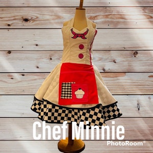 May include: A white and red chef apron with a black and white checkered skirt. The apron has a pink bow, two buttons, and a cupcake design. The text "Chef Minnie" is written below the apron.