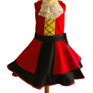 May include: A red and black dress with a yellow and black stripe on the bodice. The dress has a white ruffle collar and a black sash. The dress is on a wooden mannequin.