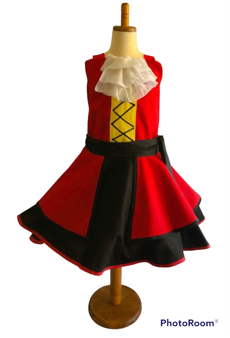 May include: A red and black dress with a yellow and black stripe on the bodice. The dress has a white ruffle collar and a black sash. The dress is on a wooden mannequin.