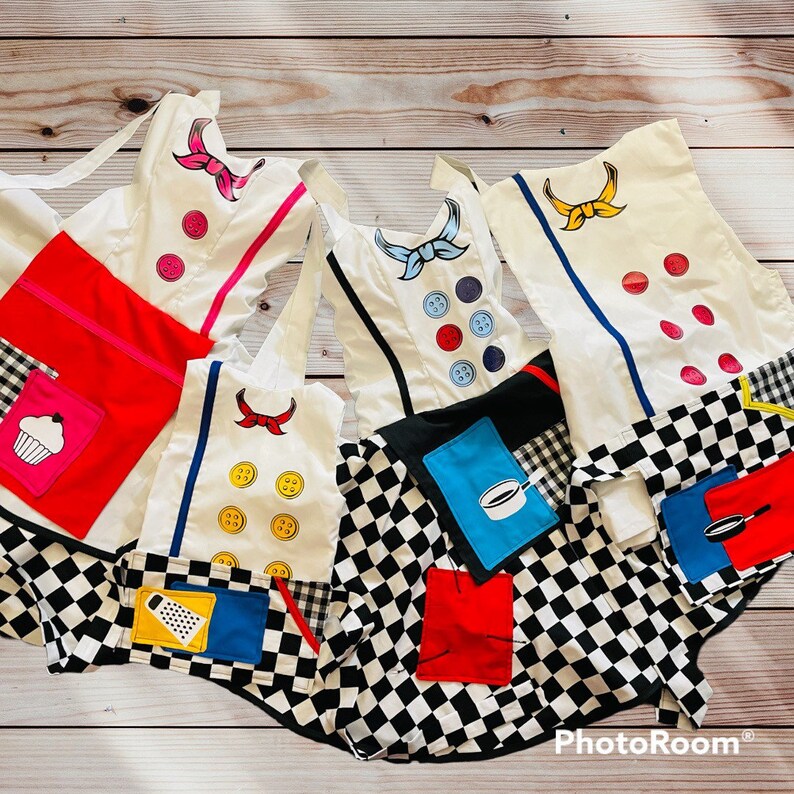 May include: Five white aprons with black and white checkered fabric and colorful patches. The patches include a cupcake, a grater, a cooking pot, a frying pan, and a button.