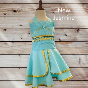 May include: A light blue dress with gold trim and coin accents. The dress has a halter neckline and a layered skirt. The text "New Jasmine" is written in white on a wooden background.