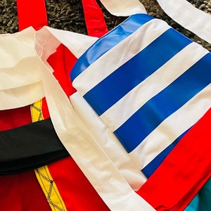 May include: A red, white, and blue striped fabric with a red and yellow trim. The fabric is folded in half and has a white fabric underneath.