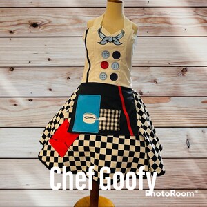 May include: A black and white checkered chef's apron with red, blue, and white accents. The apron has a pocket with a black and white checkered pattern and a blue pocket with a cartoon image of a pot and a spoon. The apron has a white top with a blue bow and black buttons. The text "Chef Goofy" is printed below the apron.