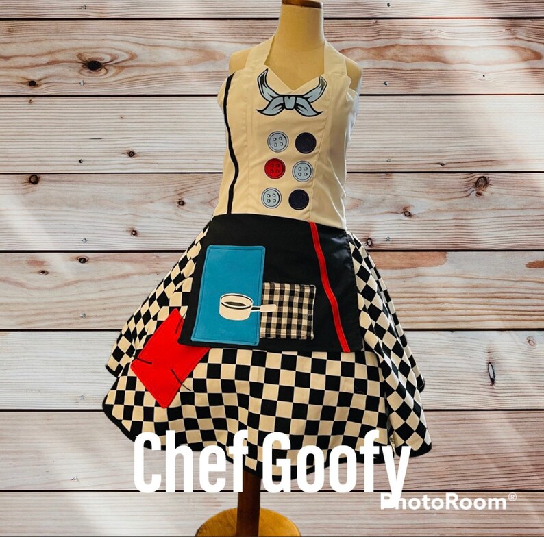 May include: A black and white checkered chef's apron with red, blue, and white accents. The apron has a pocket with a black and white checkered pattern and a blue pocket with a cartoon image of a pot and a spoon. The apron has a white top with a blue bow and black buttons. The text "Chef Goofy" is printed below the apron.