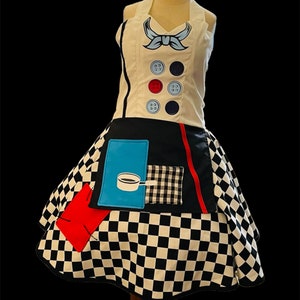May include: A white apron with a black and white checkered skirt. The apron has a blue bow, red and blue buttons, and a blue pocket with a coffee pot graphic.