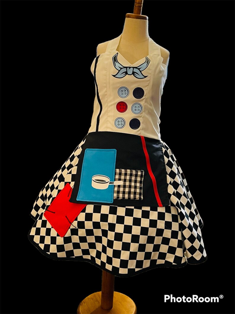 May include: A white apron with a black and white checkered skirt. The apron has a blue bow, red and blue buttons, and a blue pocket with a coffee pot graphic.