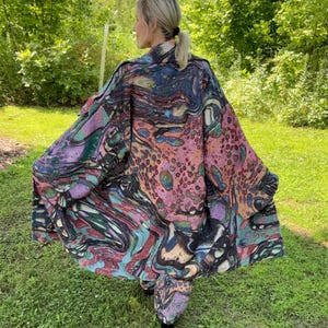 May include: A long, loose-fitting coat featuring an intricate, multicolored abstract pattern with swirls of pink, blue, black, and green. The garment has a wide collar, long sleeves, and a flowing silhouette that extends to the mid-thigh area.