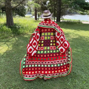 May include: A vibrant, handmade crochet coat in a patchwork design. The coat features a red base with squares of white, green, yellow, and red, and is trimmed with green and red borders. The sleeves have white squares with red rose details.