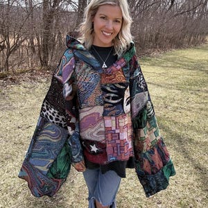 May include: A patchwork hooded jacket with a variety of patterns and colors, including blue, green, purple, and tan. The jacket has a loose fit and a hood. The person is wearing blue jeans with ripped knees.