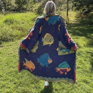May include: A navy blue throw blanket or wrap with a colorful fish pattern. The blanket has a fringed edge with red, green, and purple accents. The fish are yellow, blue, orange, and green.