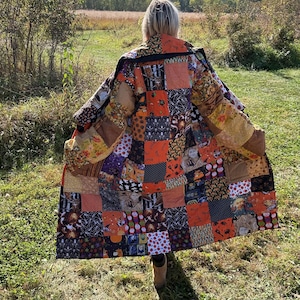 May include: A patchwork coat featuring a mix of Halloween-themed fabric squares in orange, black, and brown. The coat is worn outdoors, with the wearer facing away from the camera. The coat's design includes images of bats, ghosts, and other spooky elements.