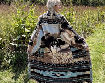 May include: A long, open-front cardigan featuring a woven tapestry design of horses in a landscape. The garment displays a color palette of black, tan, and light blue with geometric patterns along the hem and sleeves, finished with a fringed edge.