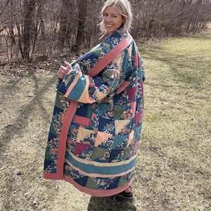 May include: A long, quilted coat in a patchwork design. The coat features a mix of colours including blue, green, peach, and burgundy. The coat has a peach-coloured trim and is worn outdoors.