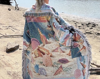 May include: A long, open-front woven cardigan featuring a colorful beach-themed pattern with various seashells, starfish, and sand textures. The garment has a fringed hem and edges, with a detailed tapestry-style design in shades of blue, tan, and pink.