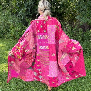 May include: A long, open-front jacket made from patchwork fabric in various shades of pink. The garment features a quilted texture with intricate, multi-colored floral and geometric embroidery patterns across the entire surface of the fabric.