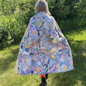 May include: A long coat constructed from a patchwork of various fabric scraps in shades of blue, yellow, pink, and white. The garment features a collared neckline, long sleeves, and a multi-patterned design composed of numerous small, irregular textile pieces.