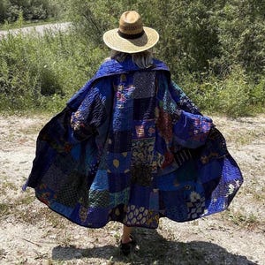 May include: A long, open-front coat made from a patchwork of various blue-toned fabrics featuring diverse patterns and textures. The garment is worn with a wide-brimmed straw hat that has a dark band around the crown, viewed from the back.