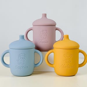 Peut inclure: Trois tasses pour bébés en silicone colorées avec couvercles et poignées. Les tasses sont de couleur bleu pastel, rose et jaune. Chaque tasse a un motif animalier différent et un nom : Sophia, Tania et Abelard. Les tasses sont conçues pour les bébés et les tout-petits.