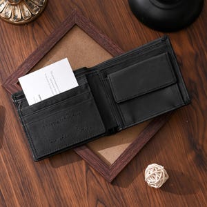 May include: Open black leather wallet with multiple compartments, including card slots and a coin pocket. The wallet has the inscription "Happy birthday, I love you - Emily" embossed on the interior. A white card is visible in one of the slots.