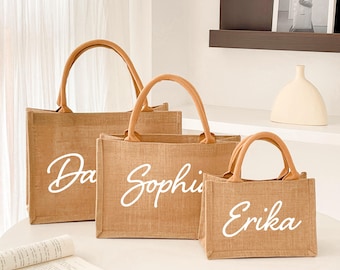 May include: Three brown burlap tote bags with leather handles. The bags are personalized with the names "Da", "Sophia", and "Erika" in white cursive lettering.