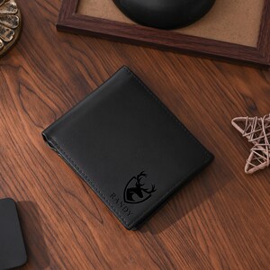 May include: A black leather wallet with a stitched border. The wallet features a deer emblem and the name "RANDY" printed on the front. The wallet is rectangular and appears to be closed.