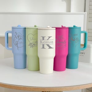 May include: Five insulated tumblers in pastel shades: light blue, light green, off-white, hot pink, and teal. Each tumbler has a handle and a lid. The tumblers are decorated with floral designs, names, and a monogram.
