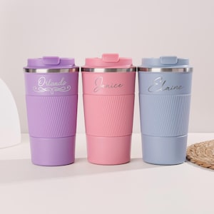Op de afbeelding: Drie gepersonaliseerde reismokken in paars, roze en blauw. Elke mok heeft een zilveren rand en deksel, met een geribbelde siliconen band. De namen "Orlando", "Janice" en "Elaine" zijn op de mokken gegraveerd.