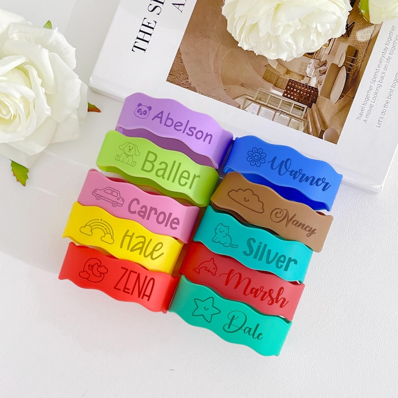 May include: A collection of colorful, wavy silicone wristbands. Each band features a different name and a small graphic, such as a car, cloud, or star. The bands are in various colors, including purple, green, blue, brown, pink, yellow, red, and teal.