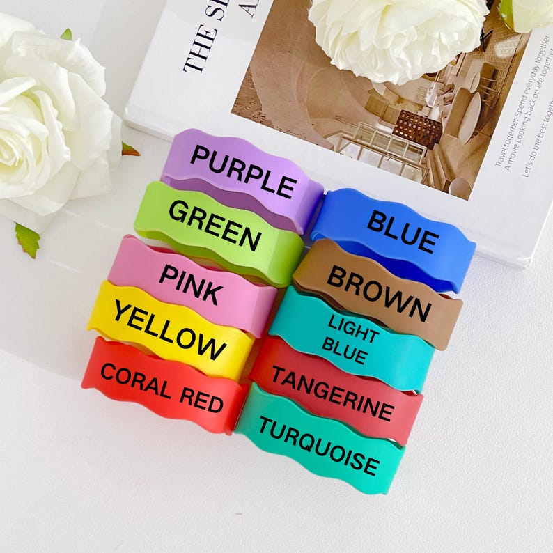 May include: A stack of colorful silicone wristbands in various colors, including purple, green, pink, yellow, coral red, blue, brown, light blue, tangerine, and turquoise. Each band has the color name printed in black.
