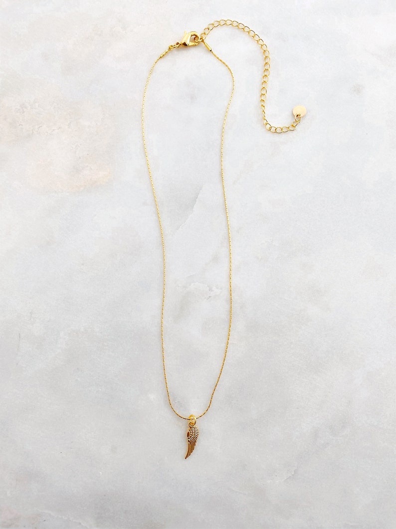 May include: A gold necklace featuring a fine chain and a wing-shaped pendant. The wing pendant is adorned with tiny, glittering details. The necklace includes an adjustable chain for a comfortable fit.