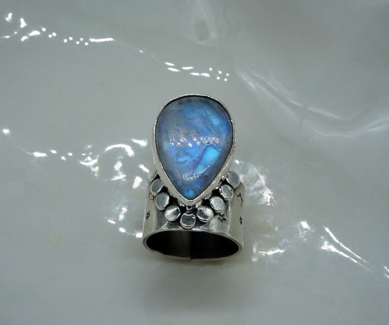Pode incluir: Um anel de prata com uma pedra de lua em forma de l&aacute;grima engastada no centro. A banda do anel &eacute; decorada com pequenas contas de prata.