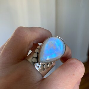 Pode incluir: Um anel de prata com uma grande pedra de lua em forma de l&aacute;grima. A pedra tem um brilho iridescente azul.