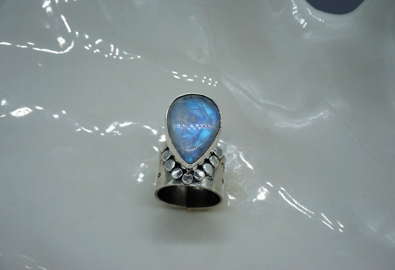 Pode incluir: Um anel de prata com uma pedra de lua azul em forma de l&aacute;grima engastada no centro. A banda &eacute; decorada com pequenas contas de prata.