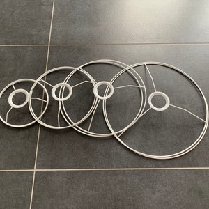 Può includere: Cinque paralumi in metallo bianco di diverse dimensioni, disposti in un motivo graduato. I paralumi sono circolari e hanno un semplice design a telaio in filo.