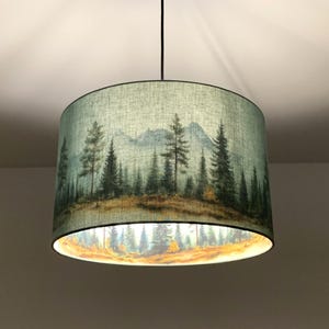 Op de afbeelding: Een groene en bruine lampenkap met een bedrukt boslandschap. De scène bevat bomen, bergen en een bewolkte lucht.