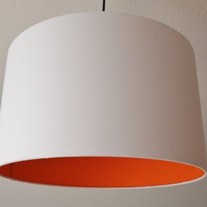 Könnte beinhalten: Weißer Lampenschirm mit orangefarbener Auskleidung. Der Lampenschirm ist rund und hat eine glatte Oberfläche.