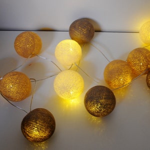 May include: A string of cotton ball lights with a warm white glow. The lights are strung together with a clear wire and are arranged in a random pattern. Some of the cotton balls are brown and some are white.