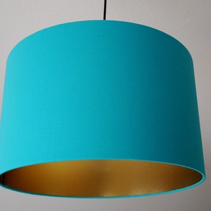 May include: A turquoise lampshade with a gold lining. The lampshade is round and has a smooth surface.