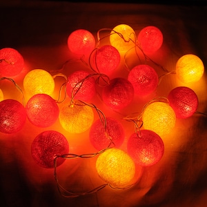 May include: A string of cotton ball lights with a mix of red and yellow bulbs. The lights are strung together with a clear wire.