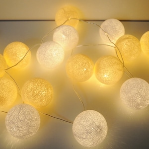 Könnte beinhalten: Eine Lichterkette mit weißen und gelben Kugeln. Jede Kugel strahlt ein weiches, warmes Licht aus. Das Arrangement erzeugt eine gemütliche und einladende Atmosphäre, ideal für dekorative Beleuchtung in Innenräumen.