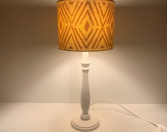 May include: A white table lamp with a white base and a yellow and brown geometric patterned lampshade.