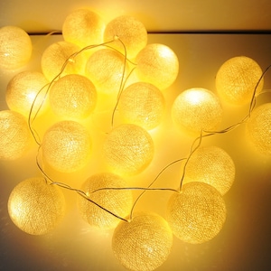 Könnte beinhalten: Eine Lichterkette mit warmweißen LED-Lichtern und Baumwollkugeln als Abdeckungen. Die Lichter sind mit einem durchsichtigen Kabel verbunden und eignen sich perfekt, um jedem Raum einen Hauch von Verspieltheit zu verleihen.