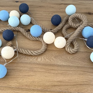 Pode incluir: Uma corda de luzes de bolas de algodão com uma corda natural, com bolas brancas, azul claro e azul escuro.