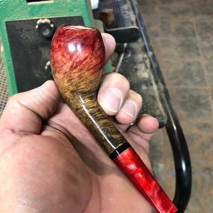 May include: A red and brown wooden smoking pipe with a black band and a red acrylic stem.