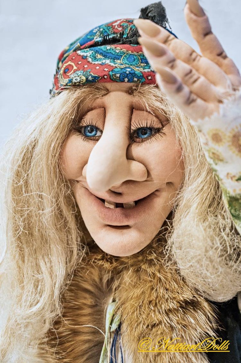 May include: A whimsical doll with long blonde hair, a large nose, and a wide smile. She is wearing a colorful bandana and a fur-trimmed jacket.