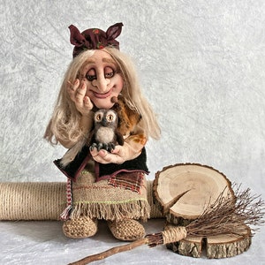 May include: A handmade doll with a brown and white owl in its arms. The doll is wearing a brown and white dress with a brown hat. The doll is sitting on a wooden platform with a broom and a rope.