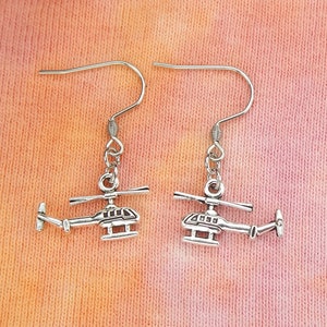 May include: A pair of silver helicopter earrings. The helicopters are detailed with a small propeller and a body.